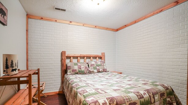 Un dormitorio con estructura de cama de madera, colcha acolchada, un banco de madera y una mesita.