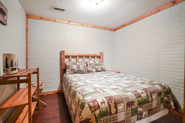 A bedroom with a wooden bed frame, a quilted bedspread, a wooden bench, and a small table.