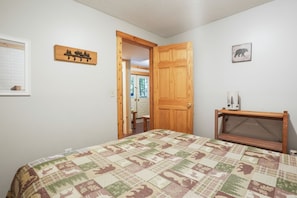 A bedroom with a quilted bedspread, a wooden door, a small table with a vase, and a wall-mounted picture.
