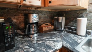 Una cocina con armarios de madera, cafetera, microondas, tostadora y dispensador de toallas de papel.