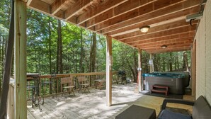 Una terraza techada al aire libre con mobiliario de madera, un jacuzzi y vistas al bosque.