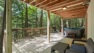 Une terrasse extérieure couverte, aménagée avec des meubles en bois, un jacuzzi et offrant une vue sur la forêt.