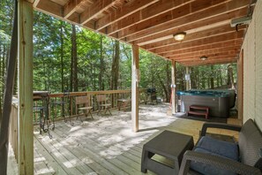 Eine überdachte Terrasse im Freien mit Holzmöbeln, einem Whirlpool und Blick auf den Wald.