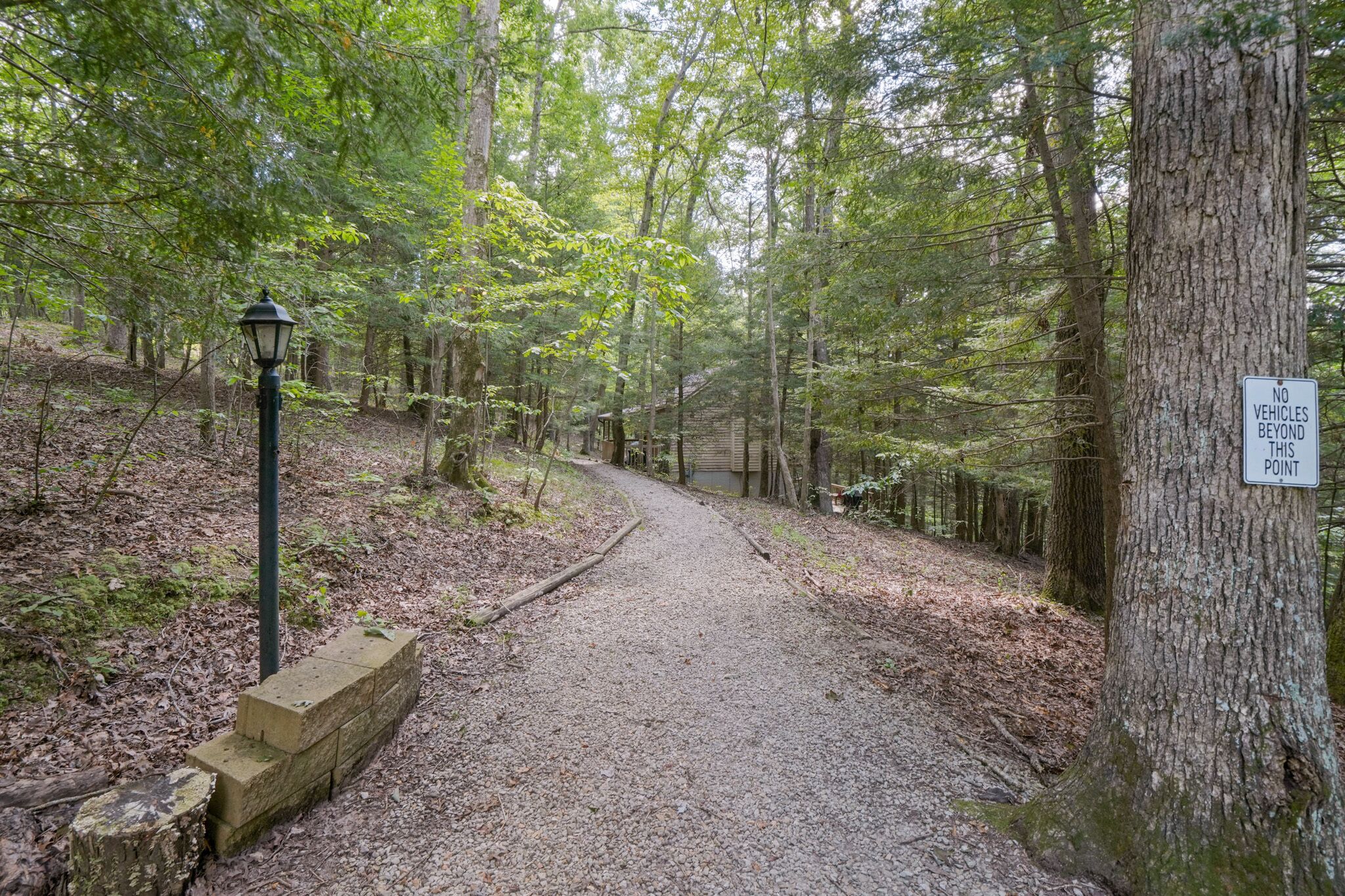 Ein Waldpfad mit Kiesweg, umgeben von Bäumen und einem Schild mit der Aufschrift 'KEINE VEHICLES BEYOND THIS POINT'.