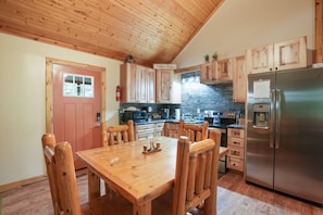 A kitchen with wooden cabinets, a stainless steel refrigerator, and a wooden dining table with chairs.