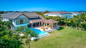 A modern two-story house with a swimming pool, a covered patio, and lush greenery.