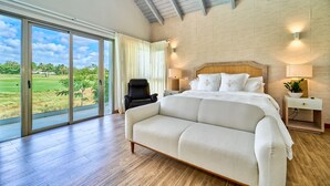 A spacious bedroom with a large bed, a sofa, and a view of a golf course through the sliding glass doors.