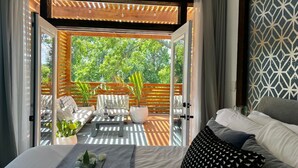 Quarto com cama, sofá e vista para área externa com móveis de madeira e plantas.