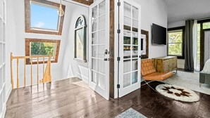 Um quarto espaçoso com escada de madeira, uma janela grande, lareira, sofá de couro e televisão.