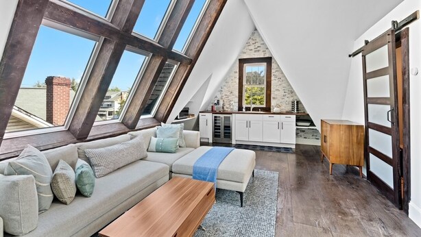 Quarto em estilo loft com um amplo claraboia, um sofá, um banco de madeira e uma área de cozinha.