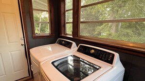 A laundry room with two front-loading washing machines, a door, and windows with a view of trees.