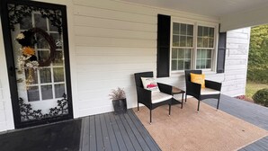 A porch with two black wicker chairs, a small table, and a decorative wreath on the door.