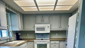 Eine moderne Küche mit weißen Schränken, einem eingebauten Backofen, einer Mikrowelle und einem Kühlschrank sowie einer Holz Arbeitsplatte.