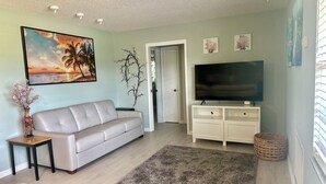Ein Wohnzimmer mit einer Couch, einem Fernseher auf einem Schrank, einem Gemälde und einer Tür zu einem anderen Raum.