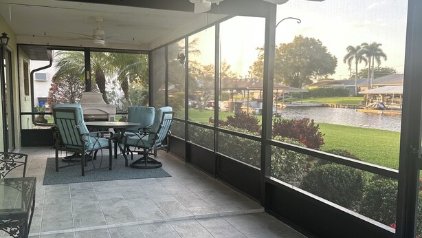 Eine überdachte Terrasse mit Tisch und Stühlen, einem Deckenventilator und Blick auf einen angelegten Garten mit einem Pool.