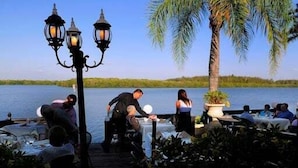 An outdoor dining area with tables and chairs, a wooden deck, and a view of a lake. - Gertrude's Siesta | Pool, Jacuzzi! 1-minute to Beach! 4-min Dining & Music! (Siesta Key)
