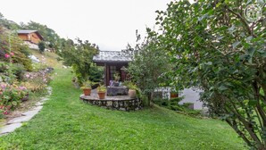 Ein gepflegter Garten mit einer kleinen Laube, umgeben von üppigem Grün und blühenden Pflanzen.