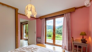 Ein Schlafzimmer mit Bett, Tisch mit Lampe und Blick auf einen Garten durch eine Schiebetür.
