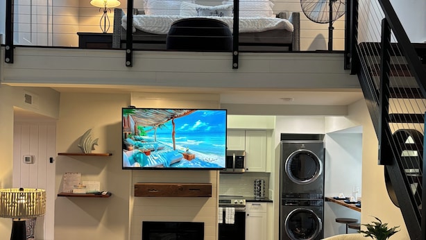 Un'ampia zona giorno con un'ampia TV a schermo piatto, un camino e una cucina sullo sfondo.