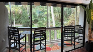 Una stanza con una porta in vetro che dà su un balcone con due sedie di legno e un tavolo.