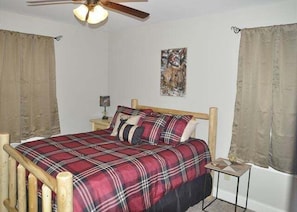 Um quarto com estrutura de cama de madeira, colcha xadrez vermelha e ventilador de teto.