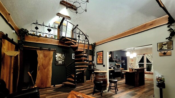 Un interior rústico con una escalera de madera, una zona de bar y una cocina visible a través de una puerta abierta.