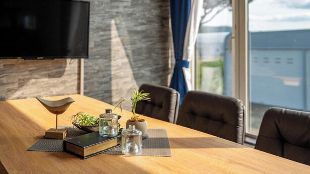 A modern conference room with a wooden table, a flat-screen TV mounted on a stone wall, and a view of the outside through large windows. - THE FURANO HIBIKI (Furano)