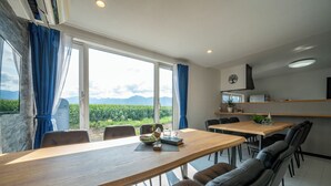 A dining area with a wooden table, leather chairs, and a view of mountains through large windows. - THE FURANO HIBIKI (Furano)