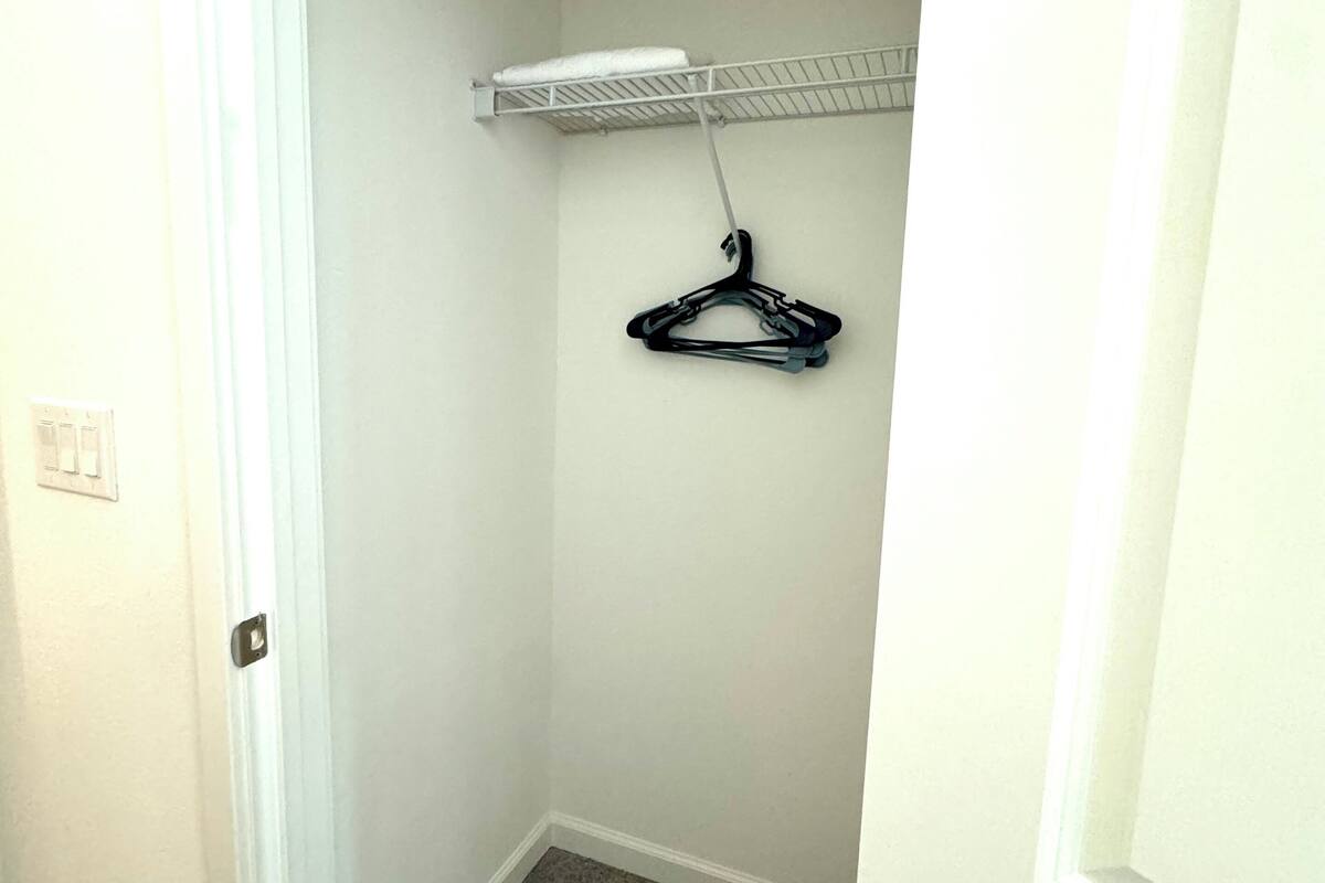 A small, narrow hallway with a white door on the left and a white wall with a metal shelf on the right.