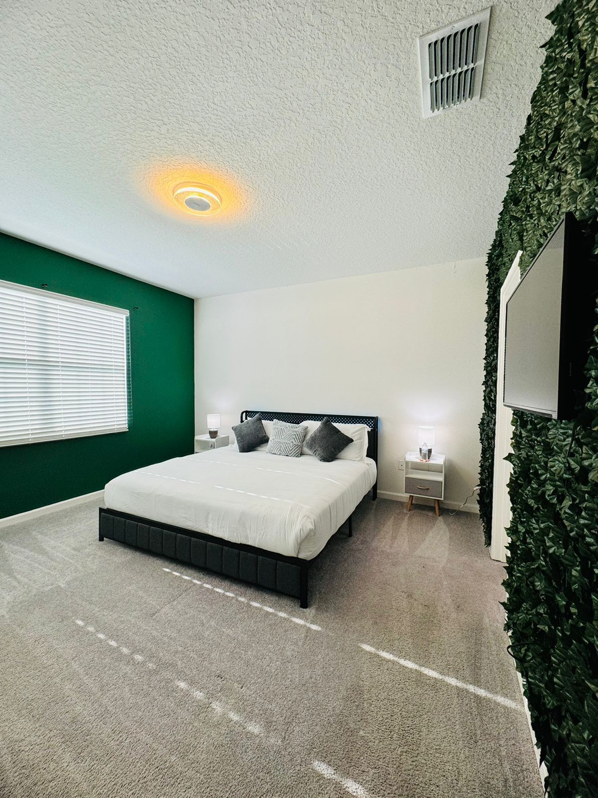 Un dormitorio con una cama, mesitas de noche, un televisor montado en la pared y una pared verde.