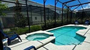 Una piscina exterior techada con dos jacuzzis, rodeada de sillas azules, bajo una estructura de techo metálico.