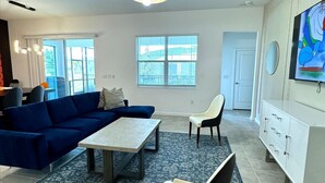 Una sala de estar moderna con un sofá azul, una mesa de centro, un sillón blanco y un televisor en la pared.