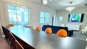 Un comedor moderno con una mesa larga, sillas anaranjadas y un televisor en la pared.