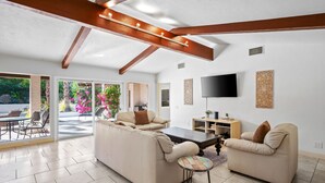 A spacious living area with a sofa set, a coffee table, and a TV mounted on the wall. - Grapevine Getaway -Large Home With Views, Pool+Spa (Palm Desert)