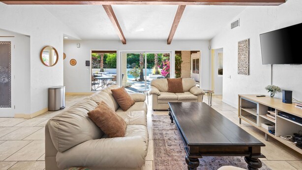 A spacious living area with two beige sofas, a dark wooden coffee table, and a flat-screen TV on a wooden stand. - Grapevine Getaway -Large Home With Views, Pool+Spa (Palm Desert)