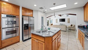 A modern kitchen with wooden cabinets, stainless steel appliances, and a granite countertop island. - Grapevine Getaway -Large Home With Views, Pool+Spa (Palm Desert)