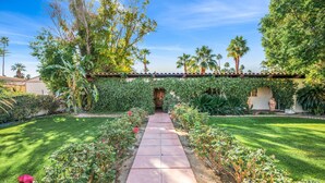 A garden pathway leading to a house with a tiled roof, surrounded by lush greenery and palm trees. - Grapevine Getaway -Large Home With Views, Pool+Spa (Palm Desert)