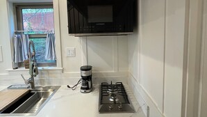 Una cocina con estufa integrada, cafetera y ventana con cortinas.