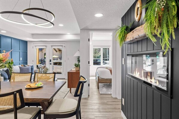 A modern kitchen with a dining area, a fireplace, and a view of the outdoors.