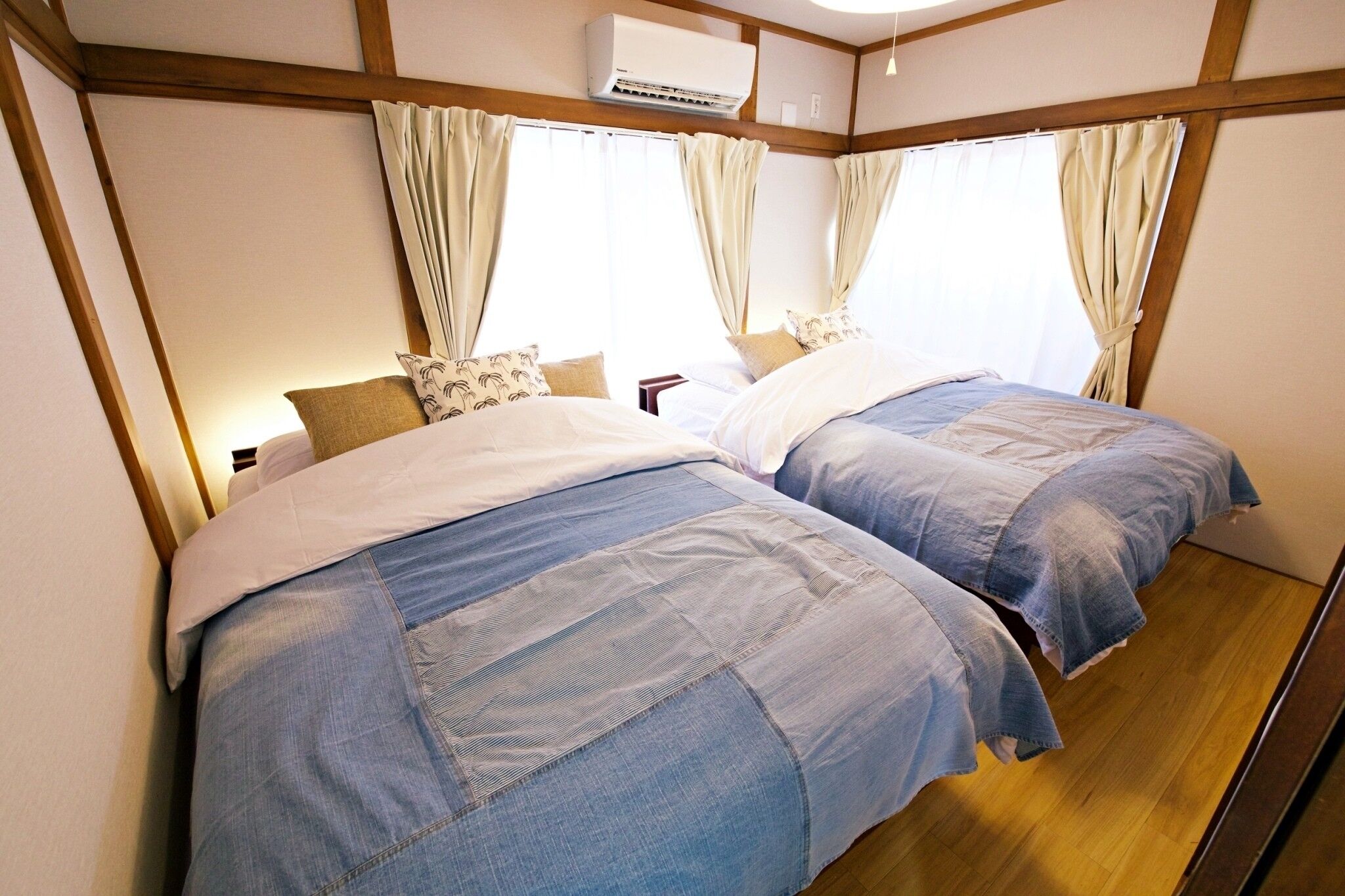 A room with two beds, wooden beams on the ceiling, and a window with curtains.