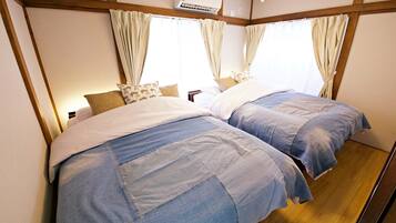 A room with two beds, wooden beams on the ceiling, and a window with curtains.