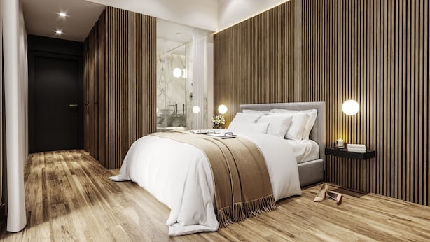 Une chambre à coucher moderne avec un grand lit, des murs recouverts de panneaux en bois et une salle de bain en marbre visible à travers une porte en verre.