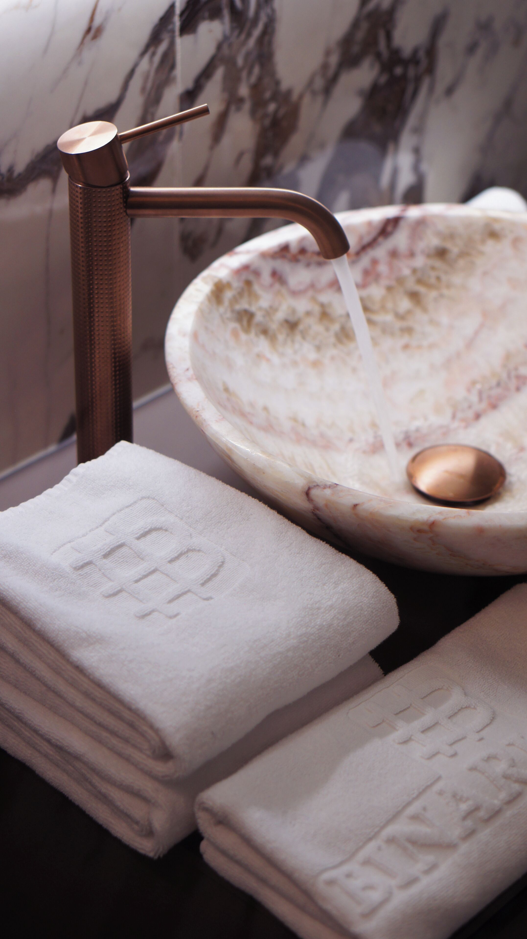 A bathroom with a marble sink, copper faucet, and stacked towels.