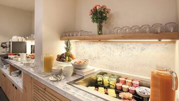 Een buffet met diverse gerechten, een fruitschaal en een sapautomaat.