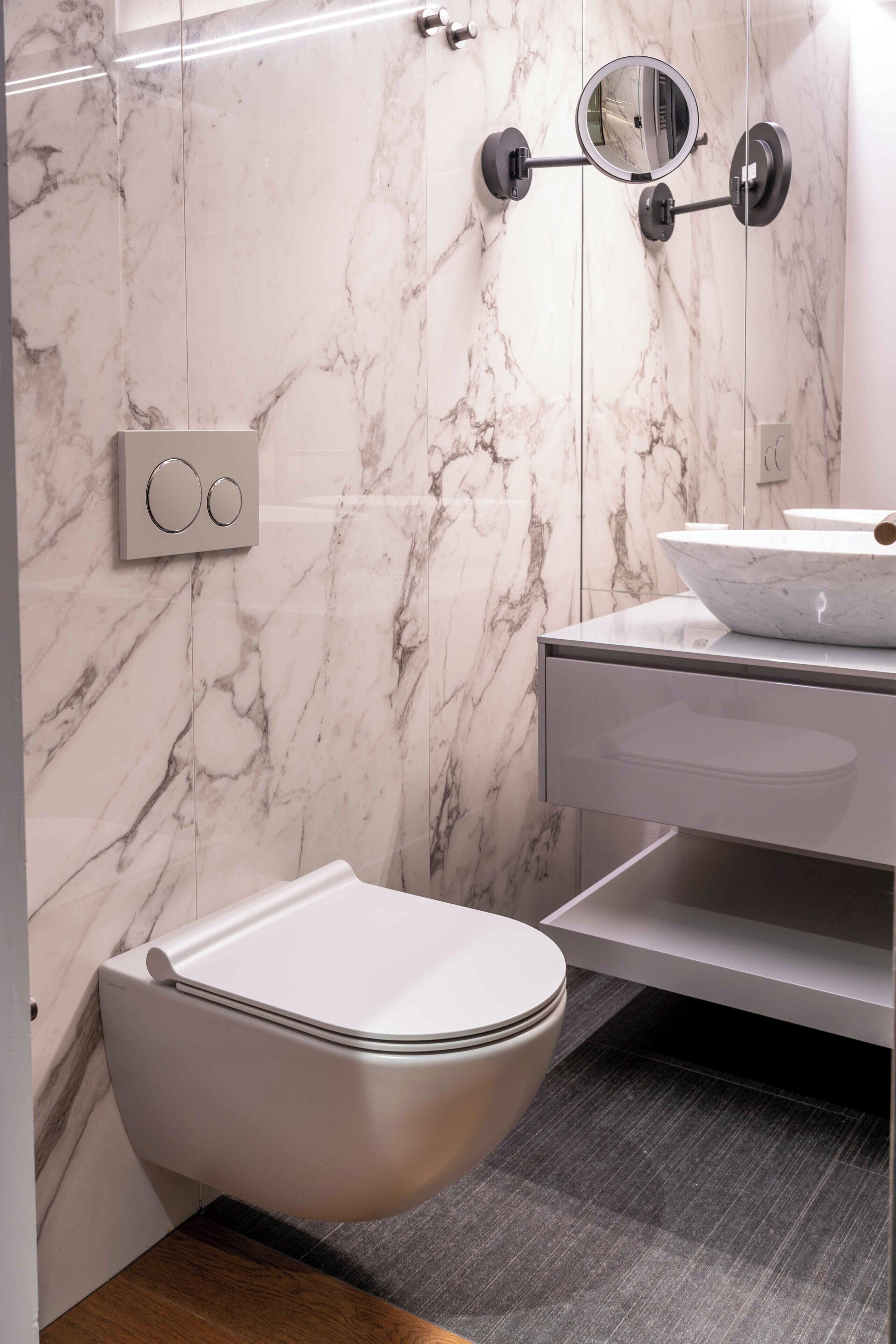 Un bagno moderno con il water, un lavandino con conca, uno specchio e pareti in marmo.