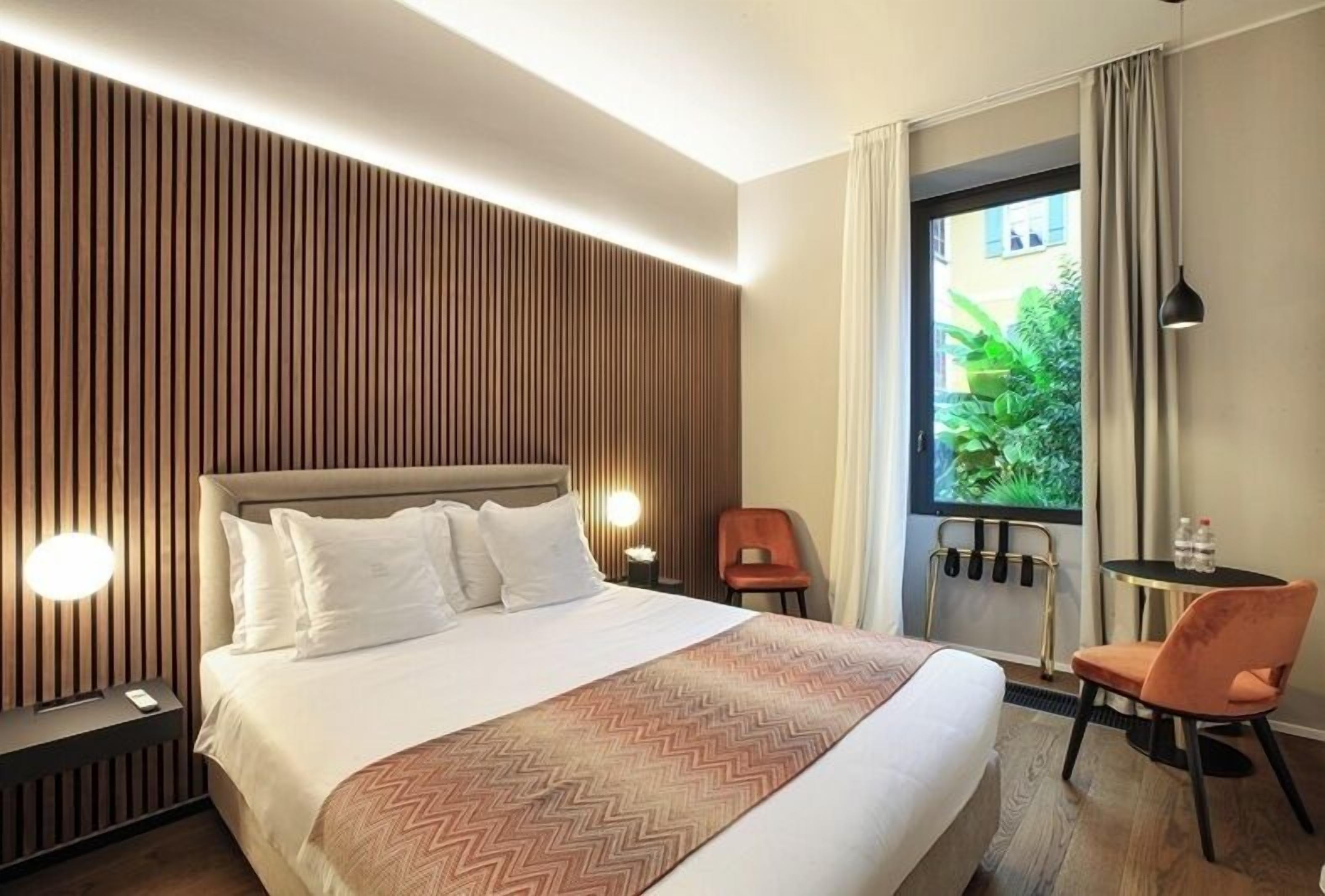 Habitación de hotel con cama, escritorio, silla, ventana con cortinas y pared con listones de madera.