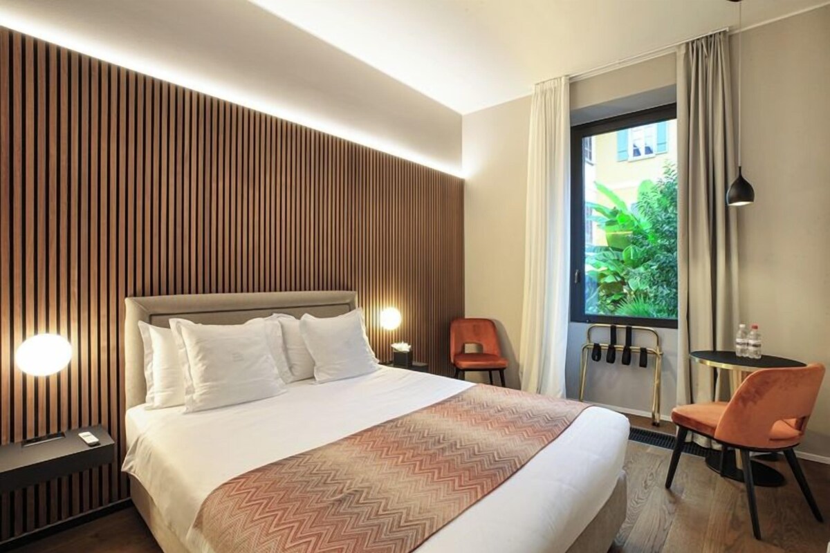 A hotel room with a bed, a desk, a chair, a window with curtains, and a wall with vertical wooden slats.