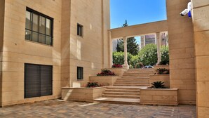 Un patio con suelo de baldosas, una escalera y un edificio con una persiana cerrada.
