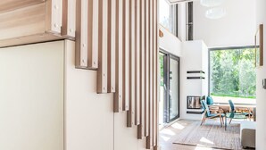 Un intérieur moderne avec un escalier, un coin repas avec des chaises et une grande fenêtre donnant sur la verdure.