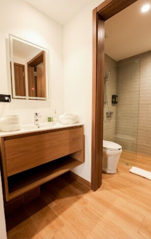Un baño moderno con tocador de madera, un espejo grande y cabina de ducha con mampara de vidrio.
